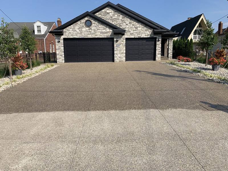 Finished exposed-aggregate concrete driveway leading to a three-car garage on a stone-front home