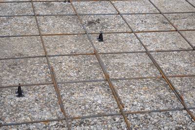 Steel rebar reinforcement grid tied on chairs over a compacted gravel base before a concrete driveway pour